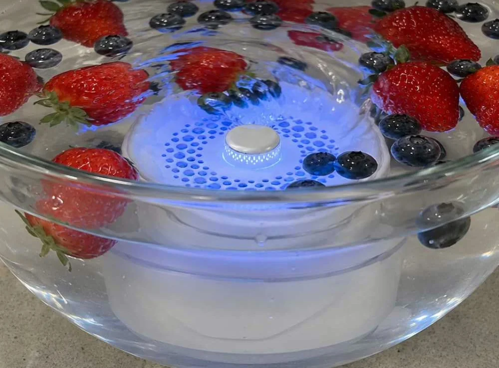 Strawberries and blueberries in a glass bowl of water with PuriEasy running underneath